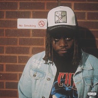 a man with dreadlocks and a hat in front of a brick wall